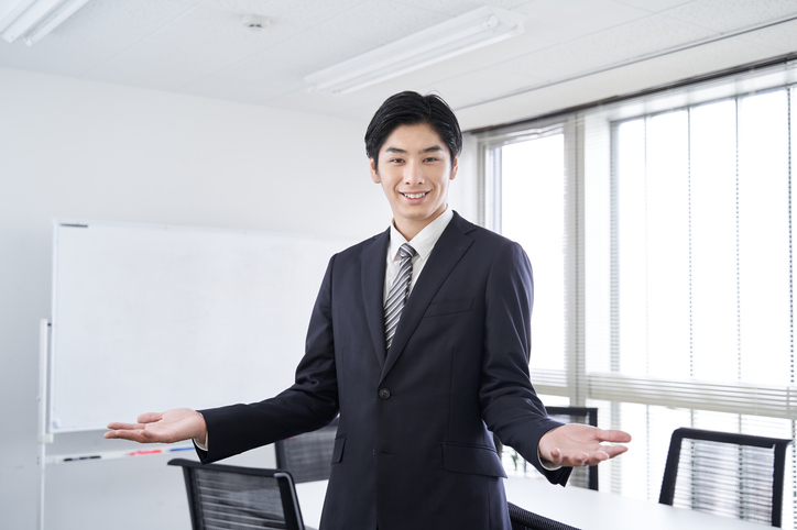 A Japanese male businessman smiles and spreads his hands in a meeting room