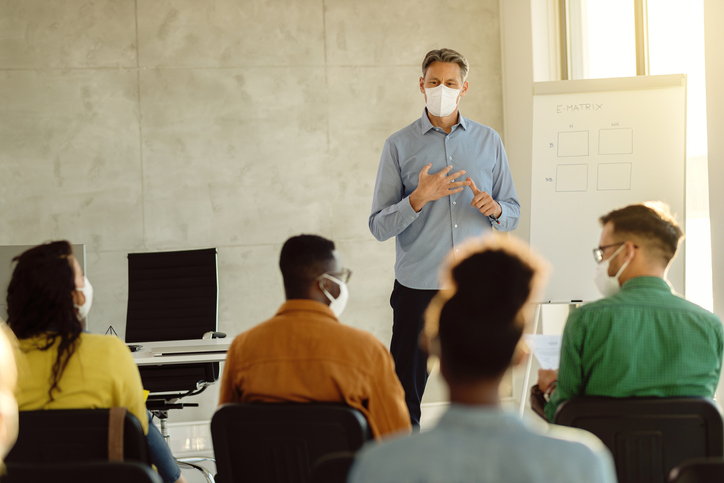 University professor wearing protective face mask while holding a class to group of students during coronavirus epidemic.