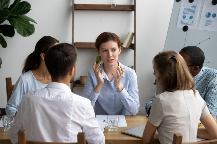 Five diverse people brainstorming sitting around desk in briefing at boardroom. Attentive multiracial employees listening company executive manager or business trainer, coaching and mentoring concept
